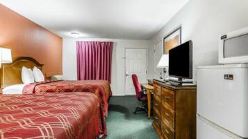 Una habitación de hotel con dos camas, un escritorio con televisor, un refrigerador y una silla roja.