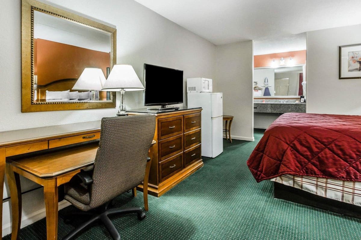 Quarto de hotel com cama, escrivaninha com cadeira, televisão, espelho, cómoda e micro-ondas.