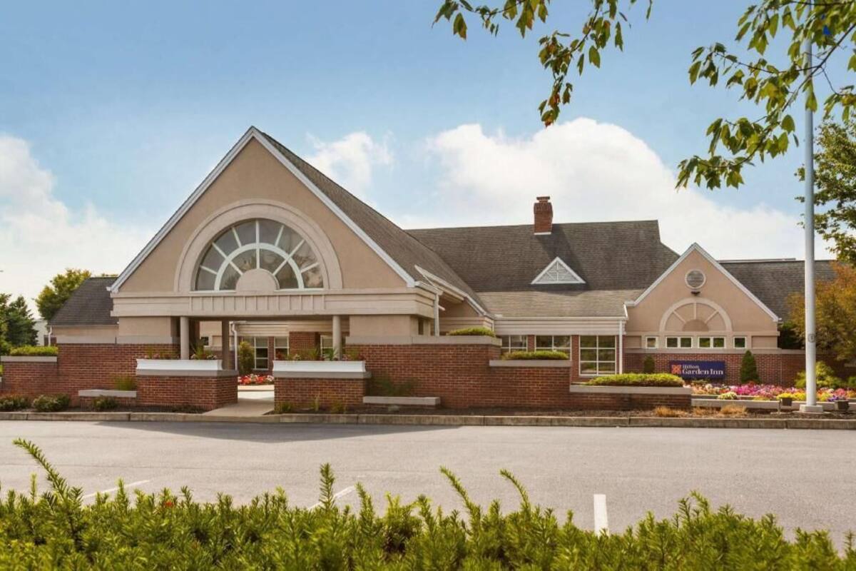 A hotel with a large central entrance, a brick facade, and a sign indicating it is a Garden Inn.