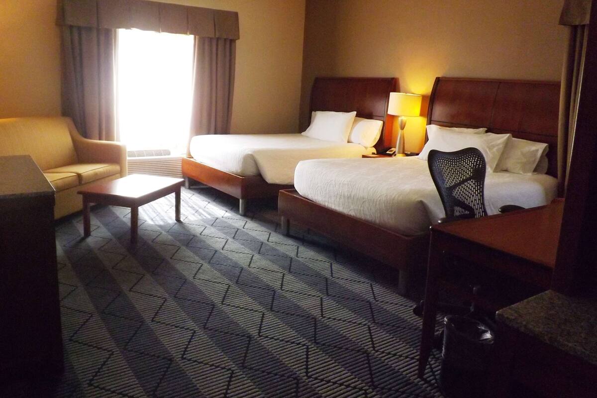 A hotel room with two beds, a sofa, a desk, and a chair.