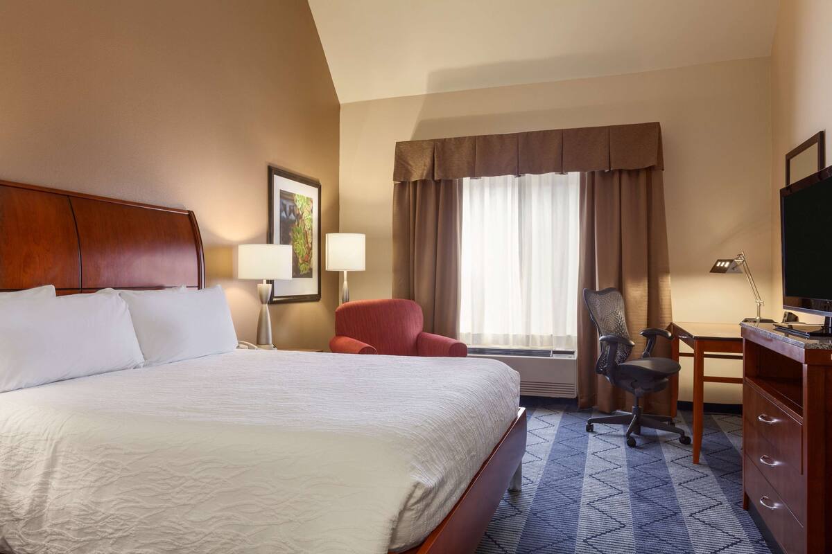 A hotel room with a large bed, a desk with a chair, a television, and a window with curtains.