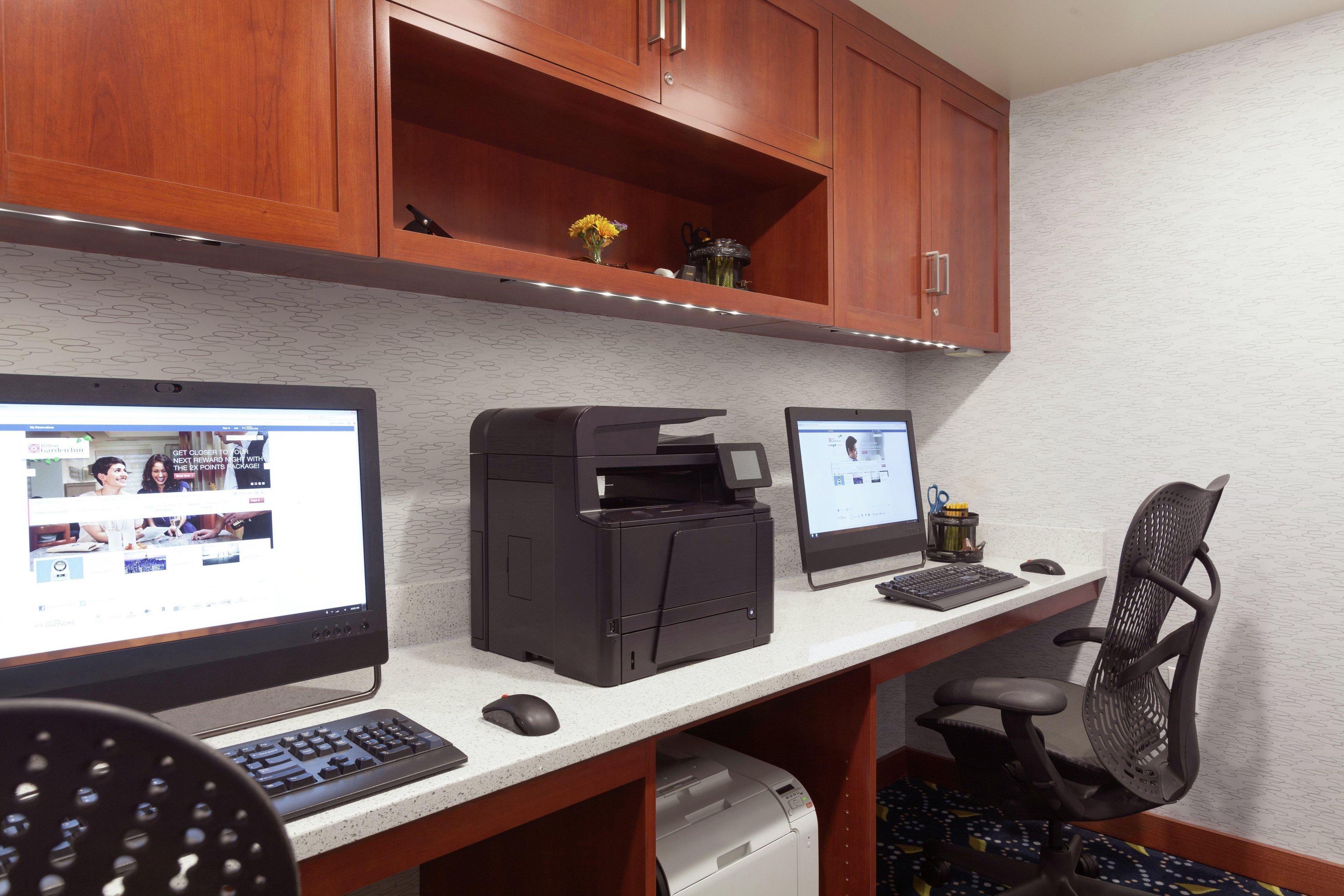 Un espace de travail équipé de deux ordinateurs de bureau, d’une imprimante et d’une chaise.