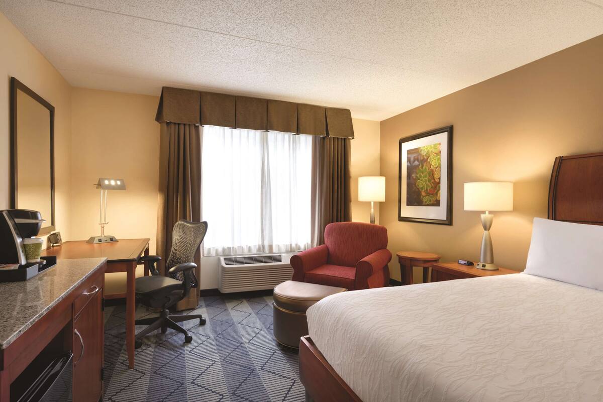 A hotel room with a bed, desk, chair, and a window with curtains.