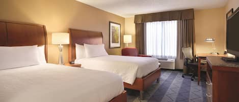 A hotel room with two beds, a desk, a chair, a television, and a window with curtains.