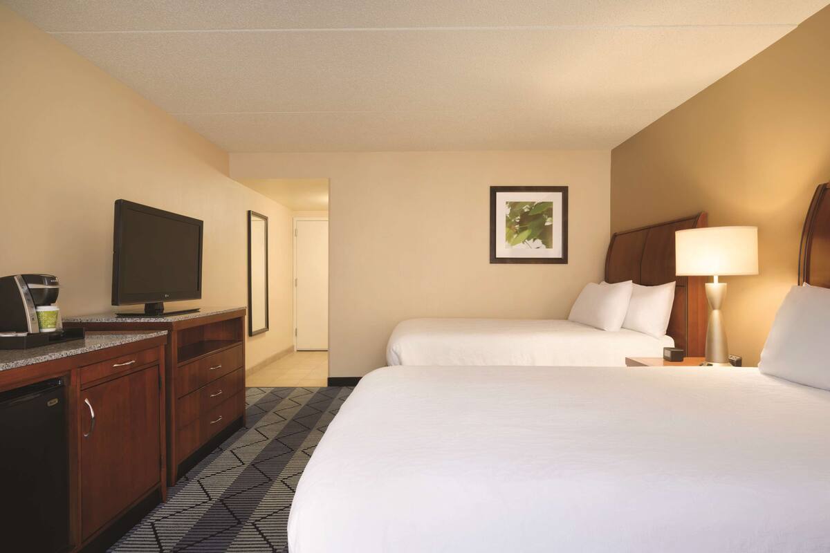 A hotel room with two beds, a TV, a desk with a coffee maker, and a framed picture on the wall.