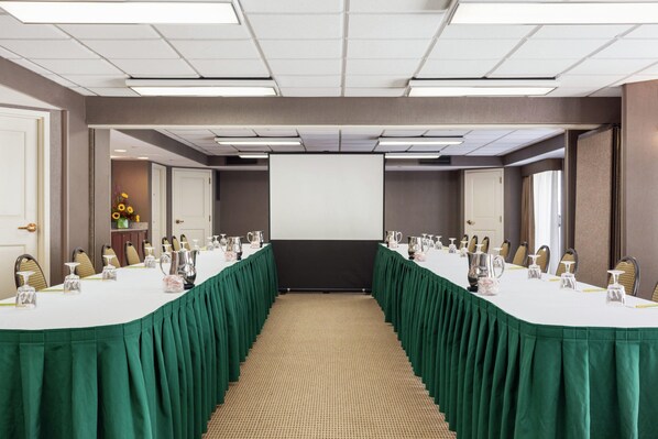 A conference room with a long table, chairs, a projector screen, and a carpeted floor.