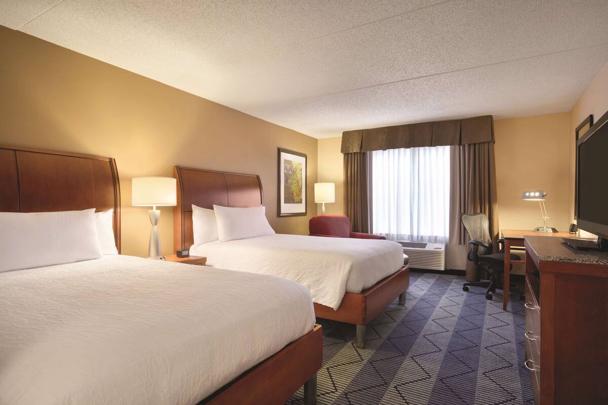 A hotel room with two beds, a desk, a chair, and a television.