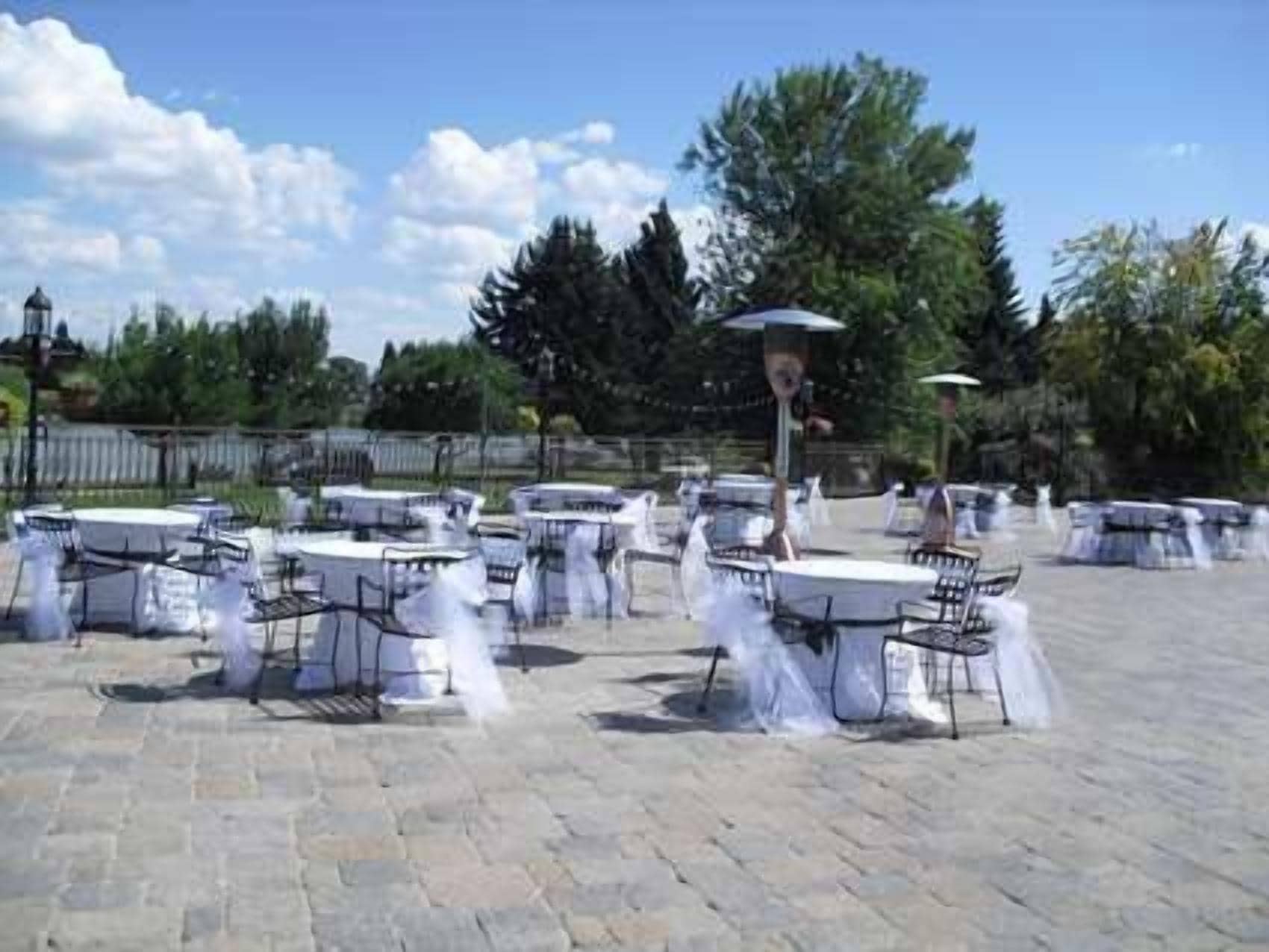 An outdoor patio with round tables and chairs, covered with white tablecloths.
