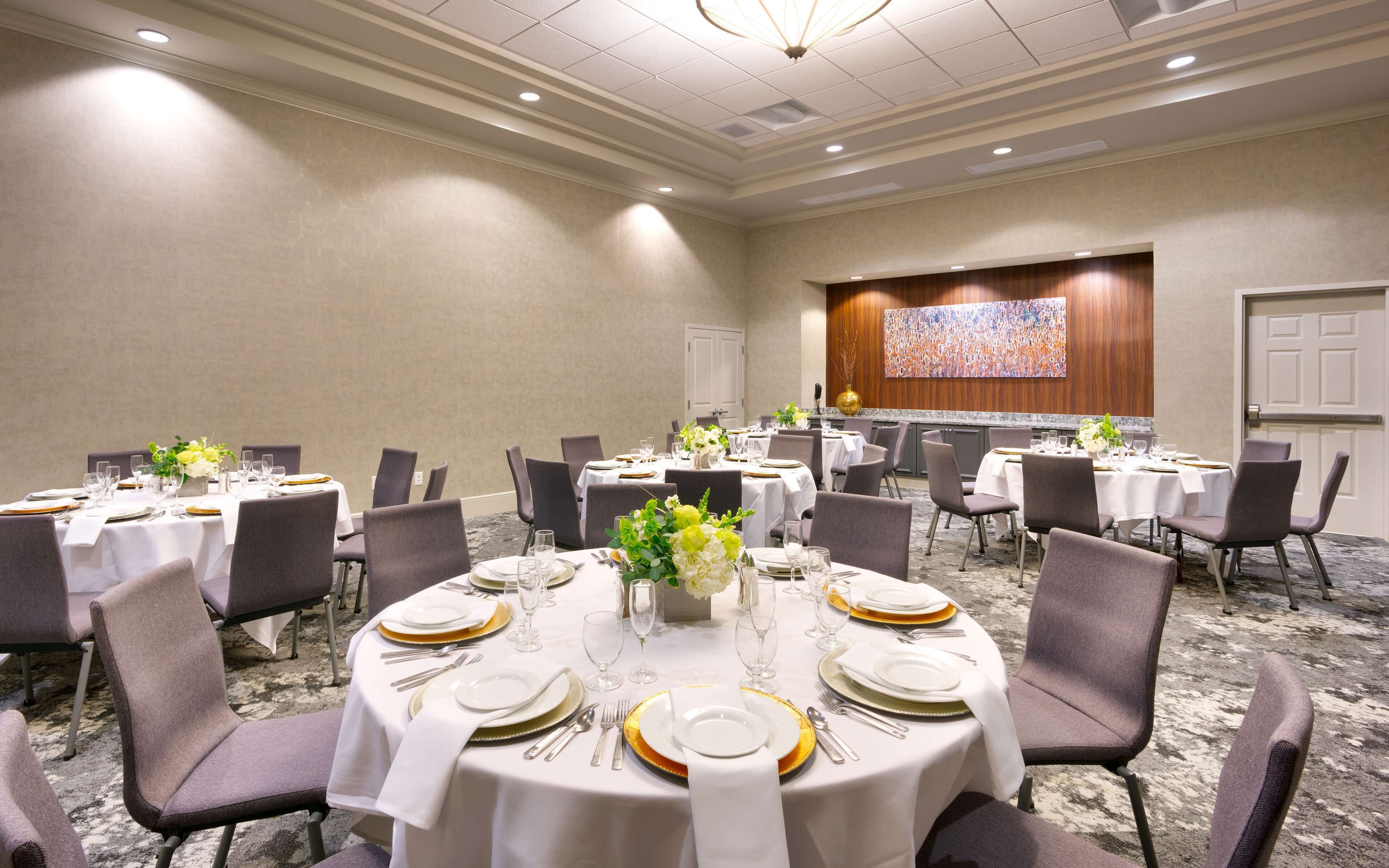 A conference room with round tables, chairs, and a large screen on the wall.
