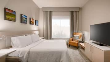 A hotel room with a bed, a desk with a chair, a television, and three paintings on the wall.
