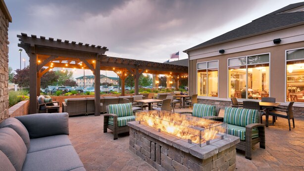 An outdoor patio area with seating, a fire pit, and a view of a parking lot and building in the background.