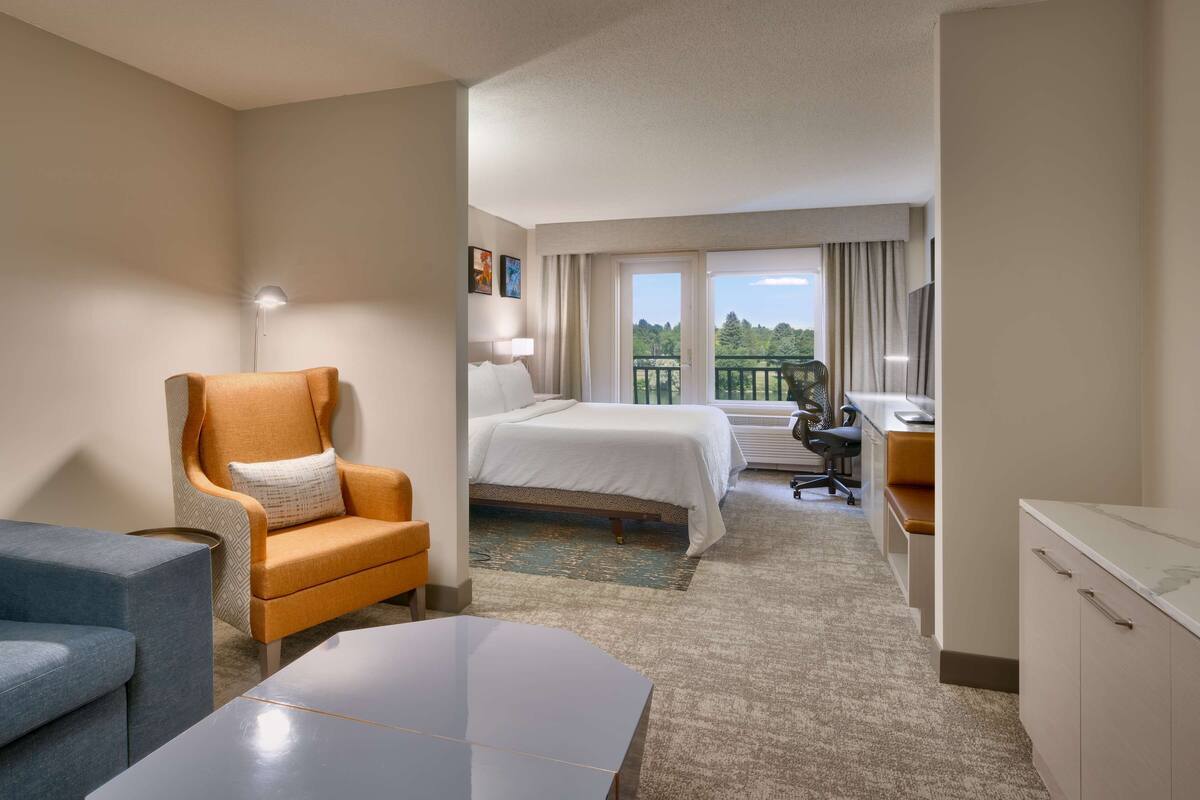 A hotel room with a bed, a desk with a chair, a sofa, and a balcony with a view.