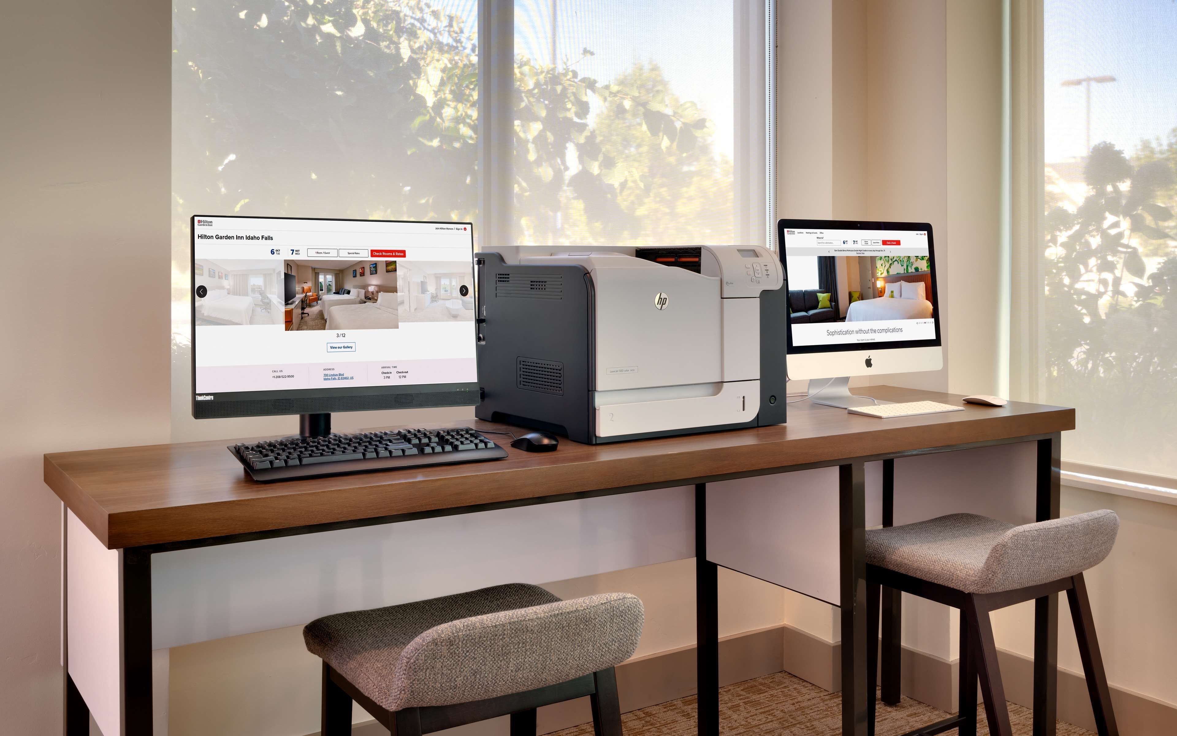 Habitación de hotel con escritorio, dos monitores, una impresora y dos sillas.