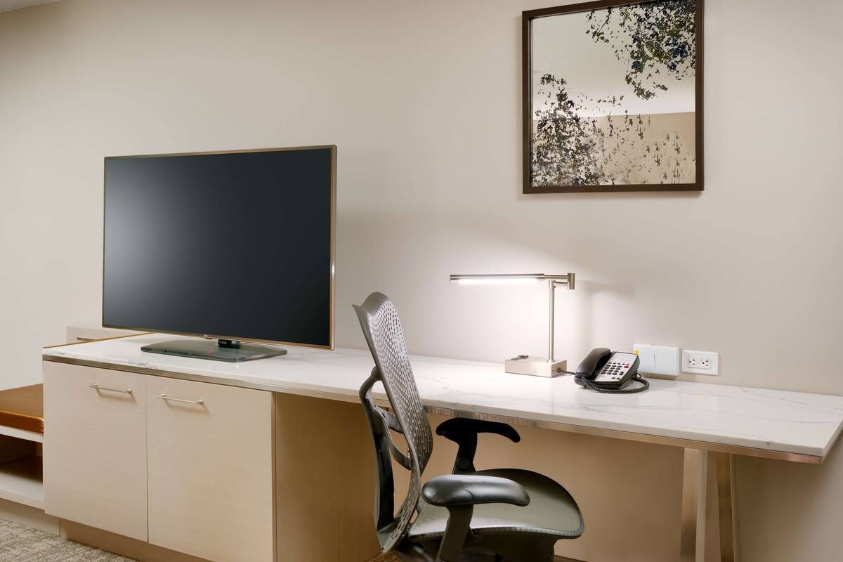 A modern office desk with a flat-screen monitor, a chair, a desk lamp, and a telephone.