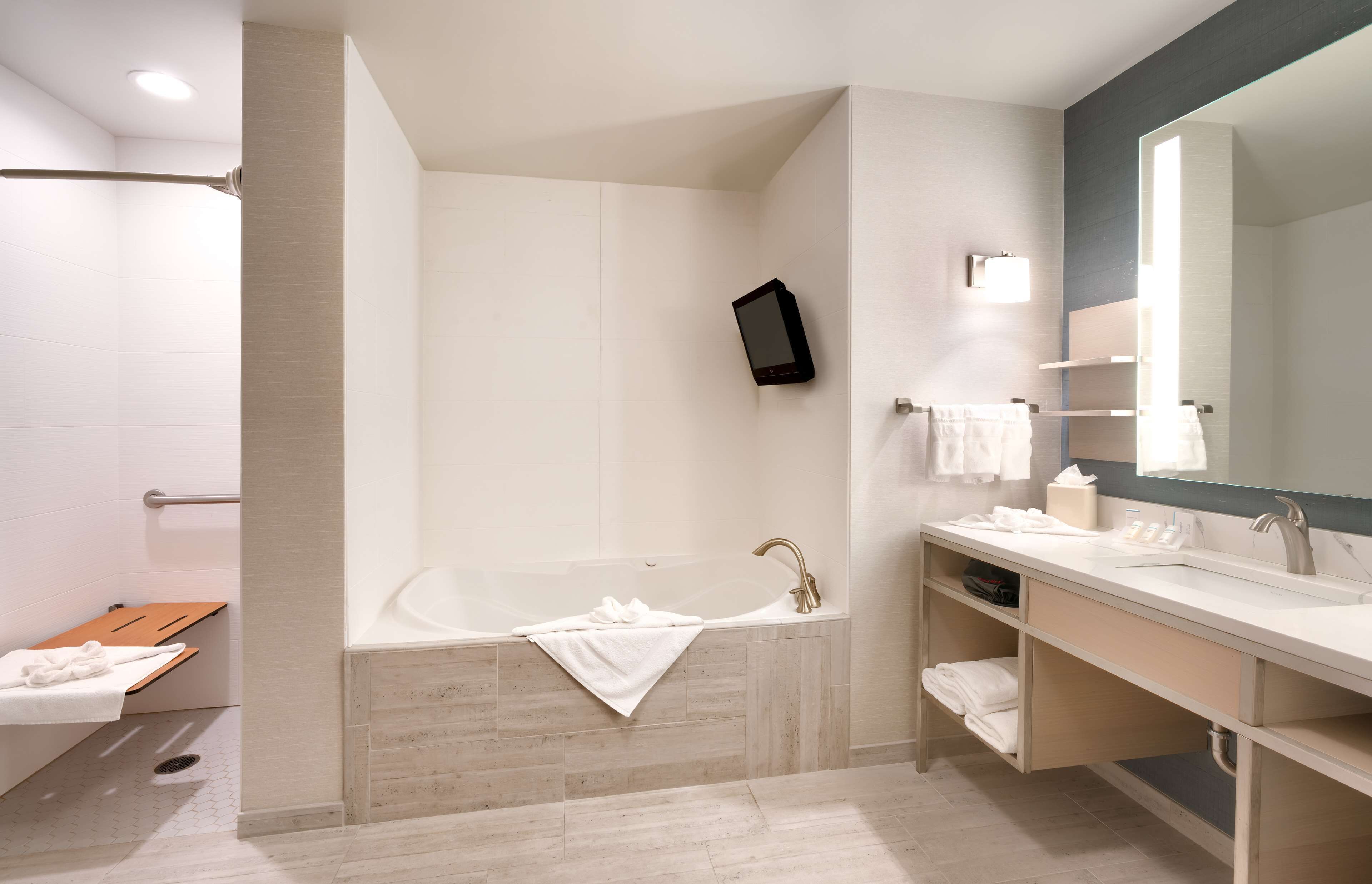 A modern bathroom with a bathtub, a large mirror, a vanity with a sink, and a shower area.