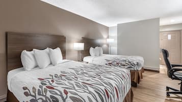 A hotel room with two beds, each with white bedding and a patterned duvet. There are two bedside lamps and a chair in the room.