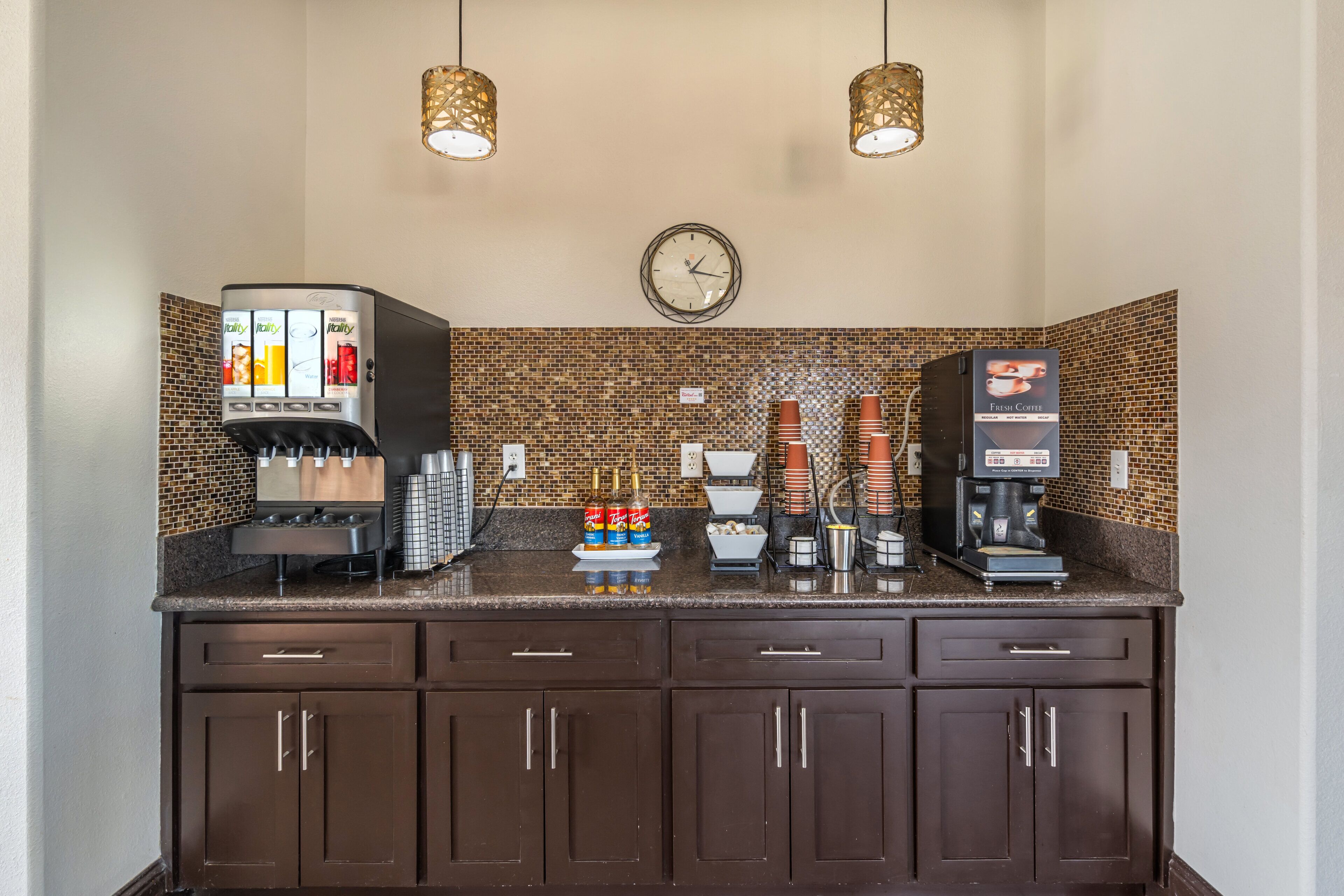 Una estación de café con una máquina de café, un dispensador de agua y un reloj en la pared.