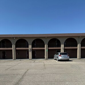 A building with multiple parking bays and a car parked in one. - Red Roof Inn & Suites Sulphur Springs (Sulphur Springs)