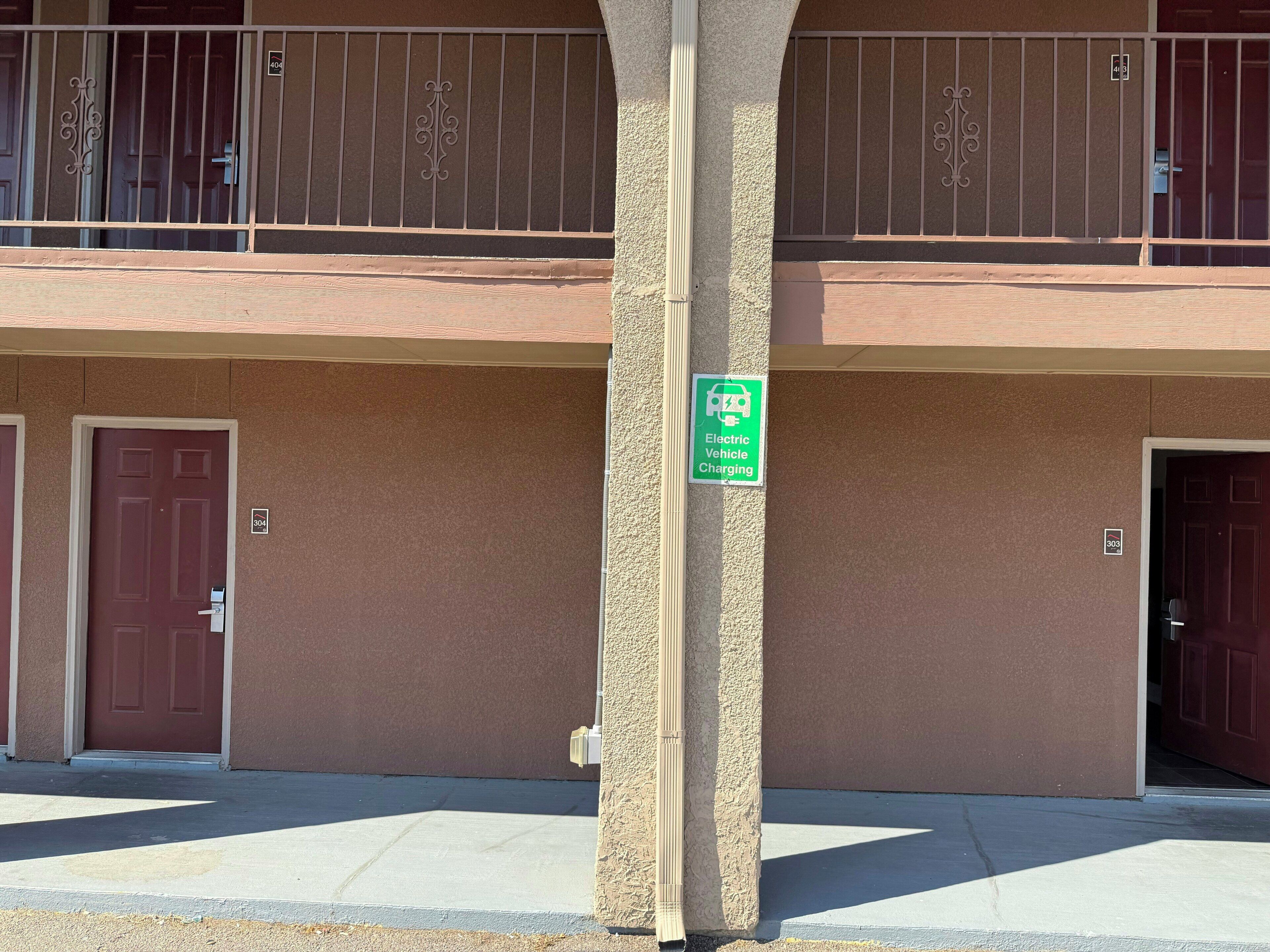 A building with a two-story balcony, a green sign indicating electric vehicle charging, and two doors with numbers 304 and 305.
