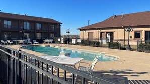 A pool area with lounge chairs and tables, surrounded by a fence. - Red Roof Inn & Suites Sulphur Springs (Sulphur Springs)