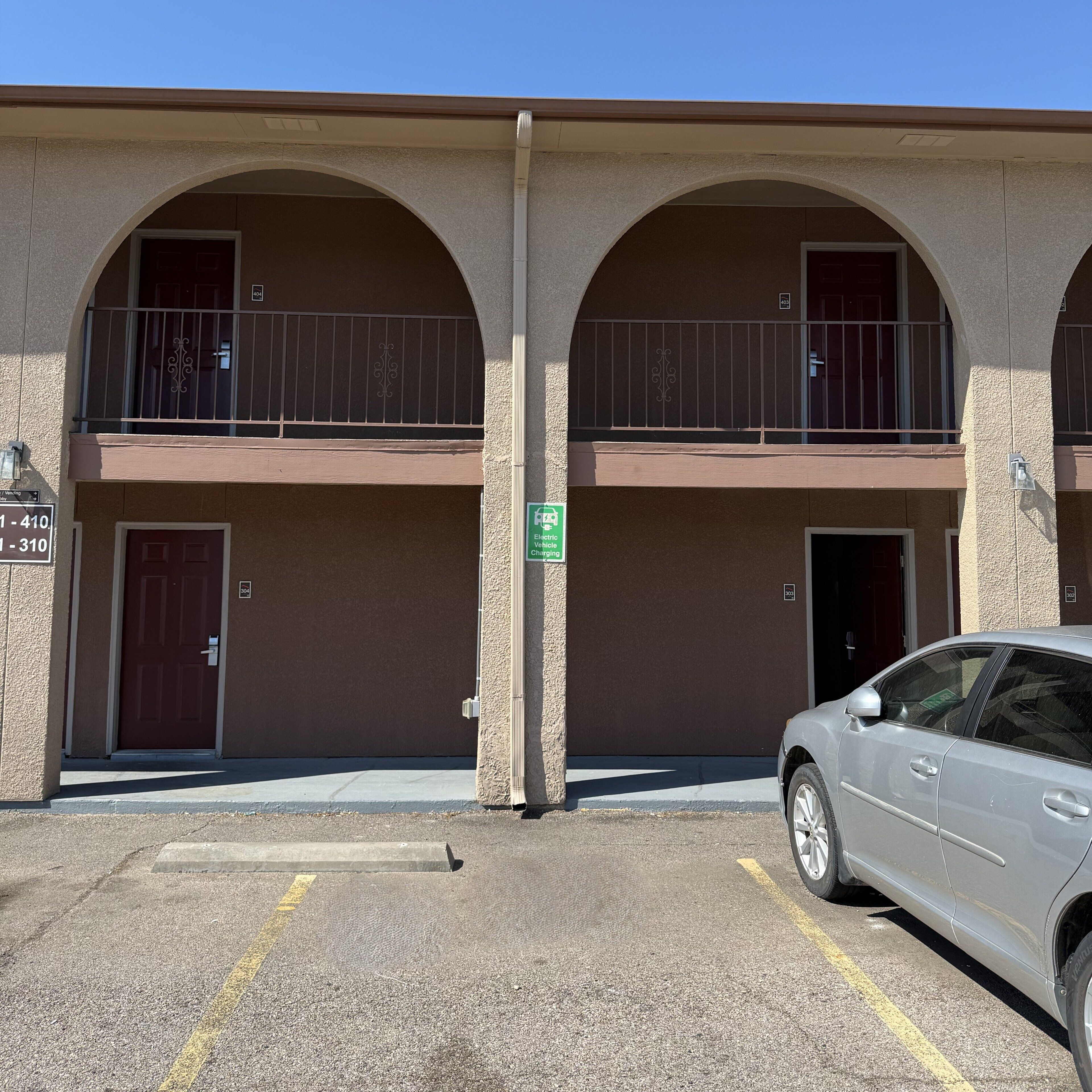 A building with two balconies, a parking lot, and a sign indicating electric vehicle charging.