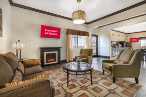 A living room with a fireplace, a sofa set, a coffee table, and a dining area with a kitchen in the background.