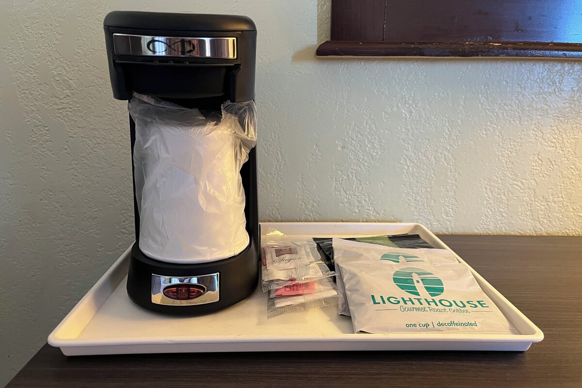 A coffee maker on a white tray with a bag of Lighthouse Gourmet Roast Coffee.