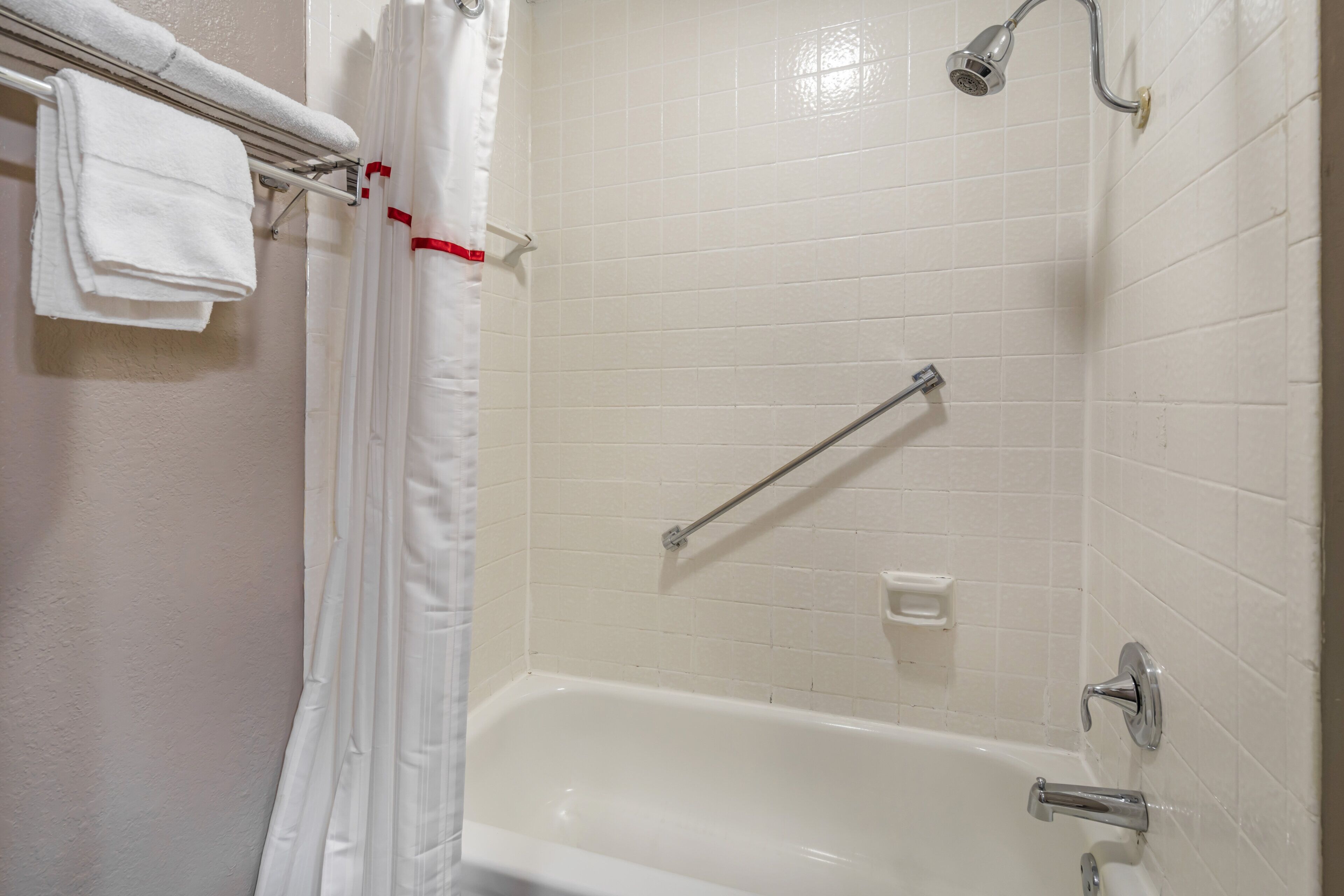 Un baño con una bañera blanca, ducha con cabezal de ducha manual y un perchero con toallas dobladas.