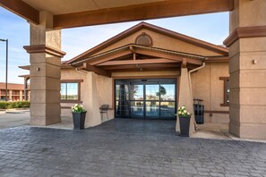 A building entrance with a covered walkway, large glass doors, and potted plants.