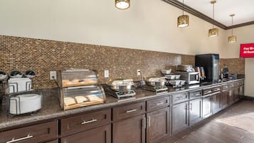 A hotel kitchen with a buffet area, a coffee station, and a sign indicating free Wi-Fi availability.