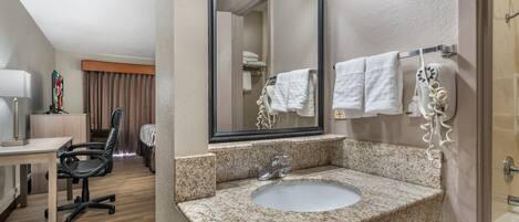 A hotel bathroom with a granite countertop sink, a large mirror, and a towel rack.
