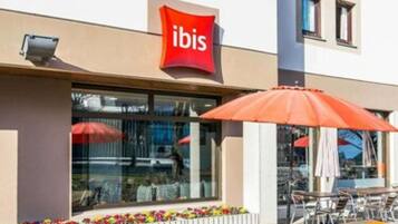 An outdoor seating area with tables and chairs, a red 'ibis' sign, and flower planters.