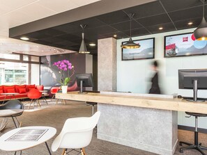 A reception area with a counter, seating, and a large window. - ibis Thonon Centre Hotel (Thonon-les-Bains)