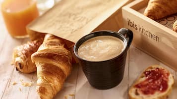 En træbakke med croissanter, en kop kaffe og et glas appelsinjuice.