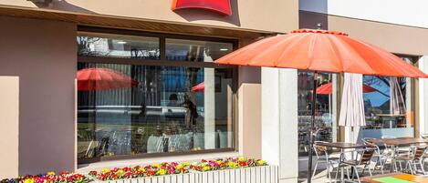 An outdoor seating area with tables and chairs, a flower bed, and a building with an 'ibis' sign.