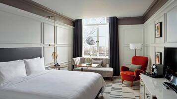 A hotel room with a large bed, a sofa, a red armchair, a desk with a lamp, and a view of a Ferris wheel.