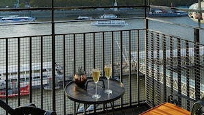 A balcony with a view of a river, a Ferris wheel, and a table with a glass of wine. - London Marriott Hotel County Hall (London)