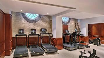 A gym with treadmills, stationary bikes, and a brick wall with windows.