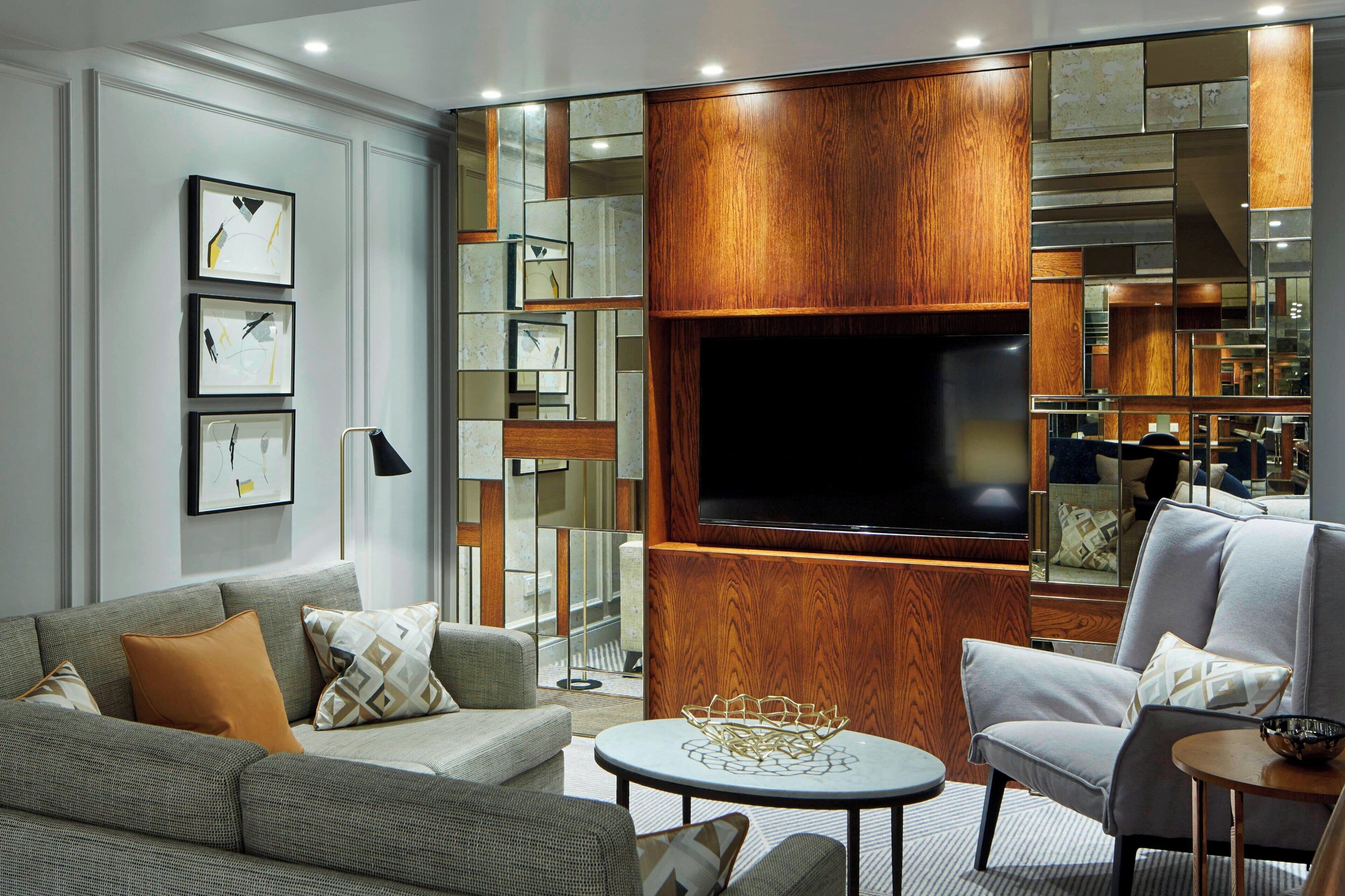 Un salon moderne avec un canapé gris, une table basse ronde et un mur décoratif en bois sur lequel est accrochée une télévision à écran plat.