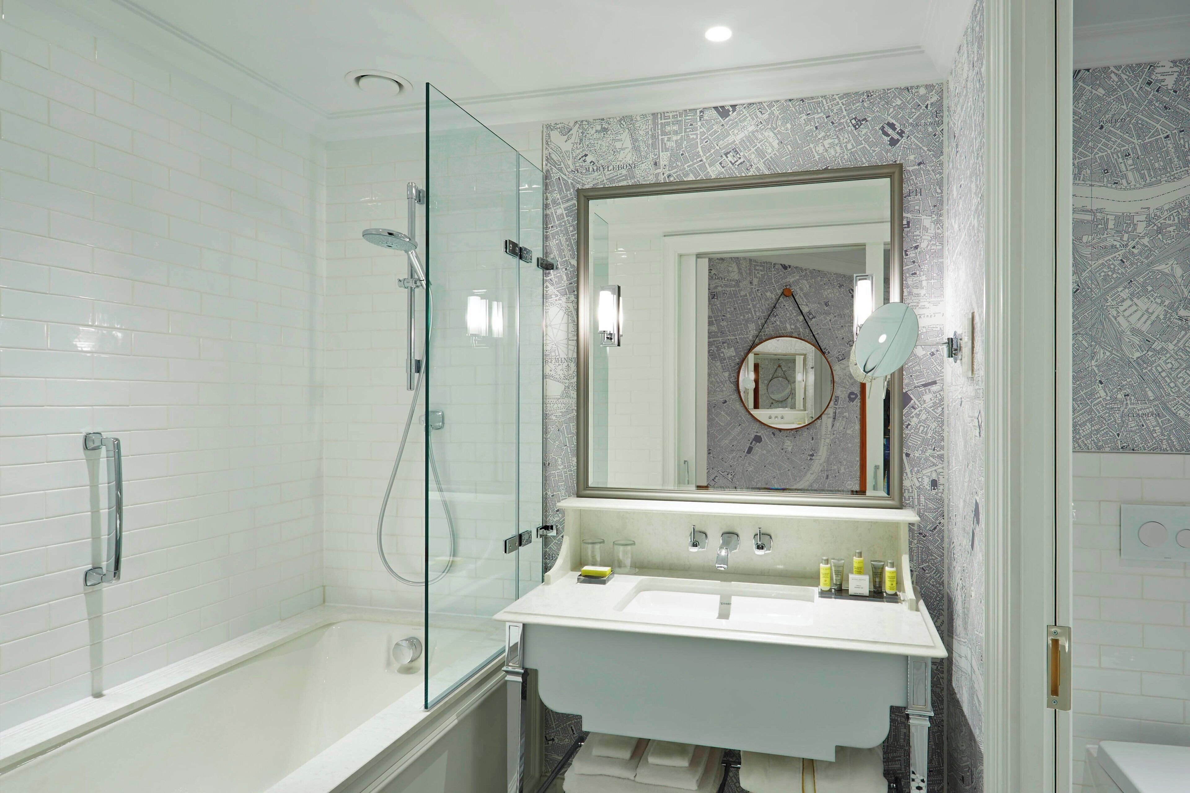 A modern bathroom with a glass-enclosed shower, a white sink with a mirror above it, and a tiled wall with a map design.