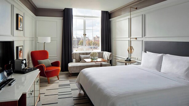 A hotel room with a large bed, a desk with a computer, a red armchair, a sofa, and a view of the city through the window. - London Marriott Hotel County Hall (London)