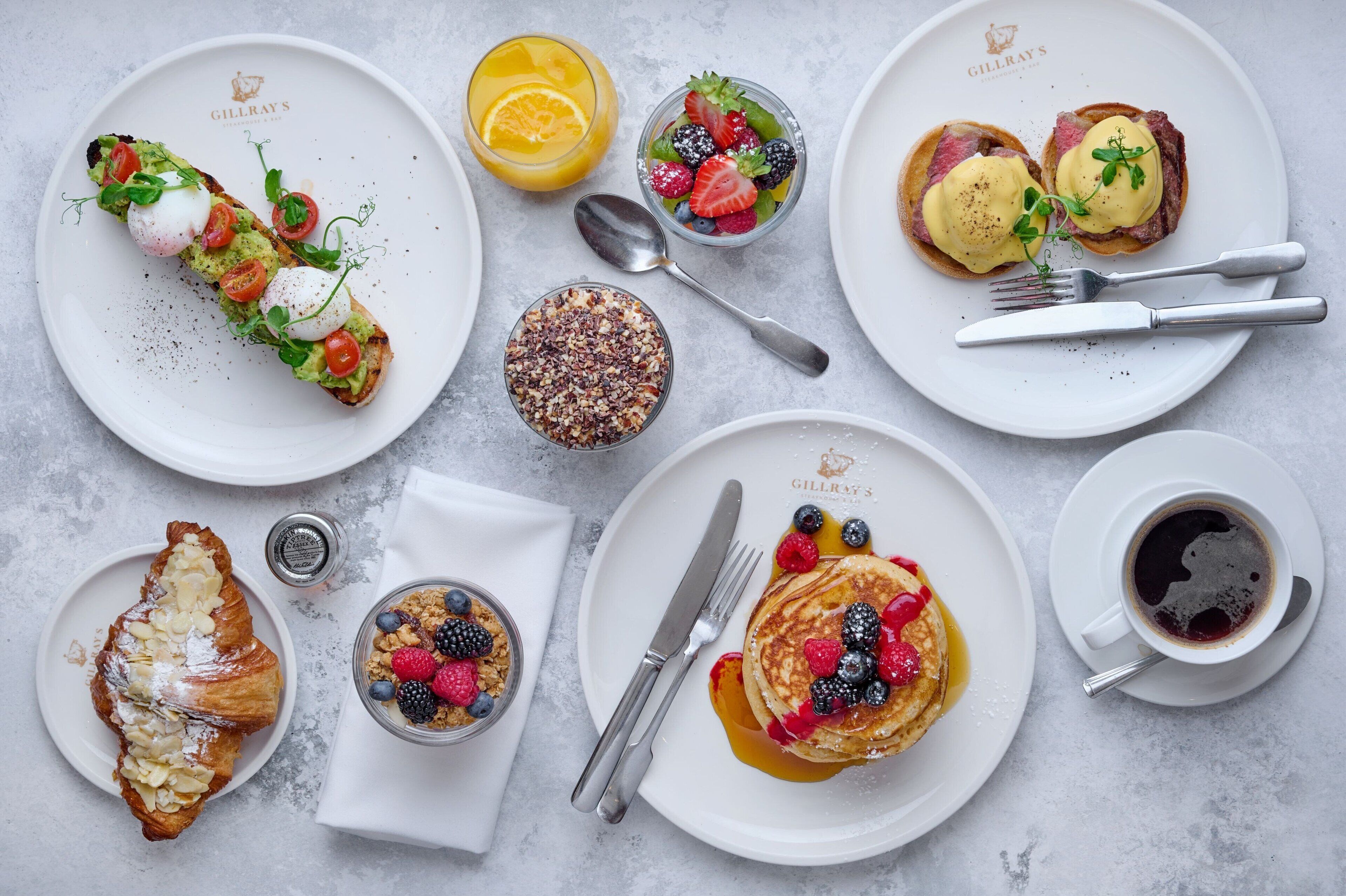 A breakfast spread with various dishes including eggs, pancakes, and pastries on white plates.