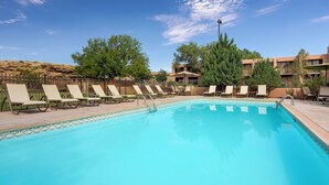 A swimming pool with lounge chairs and a table, surrounded by trees and buildings.