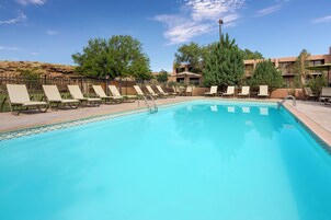Una piscina con sillas de descanso y una mesa, rodeada de árboles y edificios.
