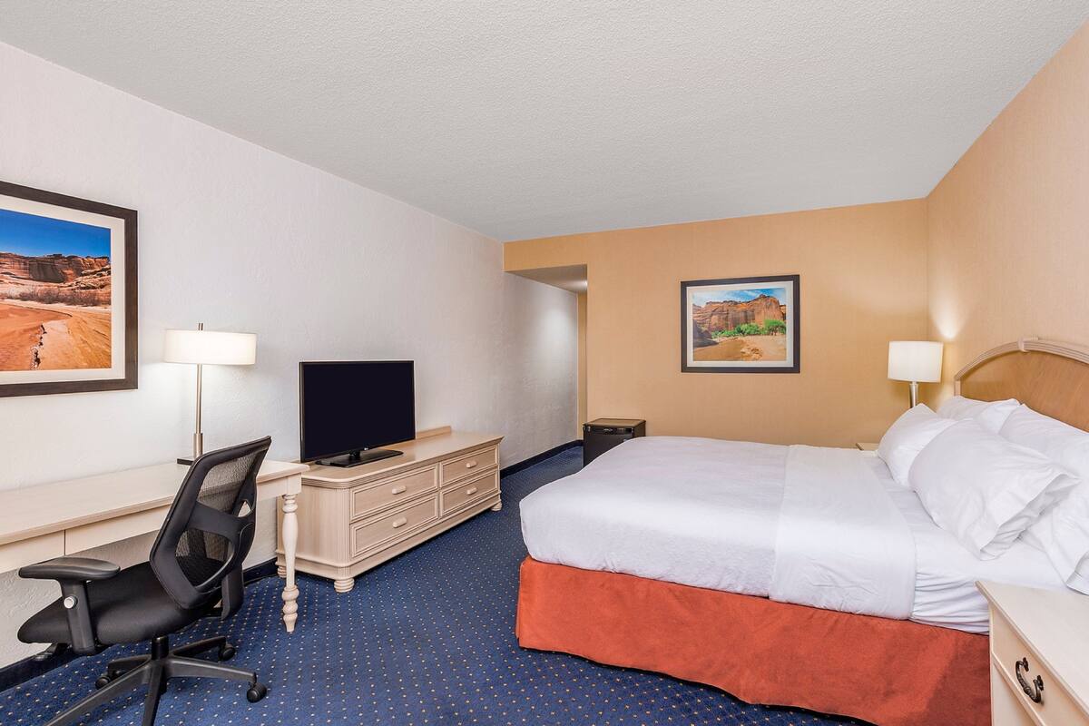 A hotel room with a bed, desk, chair, television, and two wall-mounted lamps.