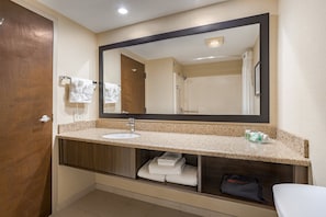Une salle de bain avec un grand miroir, un lavabo et une douche. On y trouve des serviettes et un sèche-cheveux sur le comptoir.