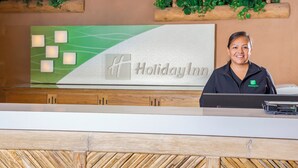 A reception desk with a Holiday Inn sign, wooden paneling, and green foliage decorations. - Holiday Inn Canyon De Chelly by IHG (Chinle)