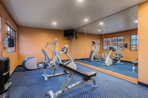 A gym with exercise equipment, a mirror, and a TV on the wall.