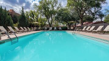 A swimming pool with lounge chairs and umbrellas, surrounded by trees and buildings.