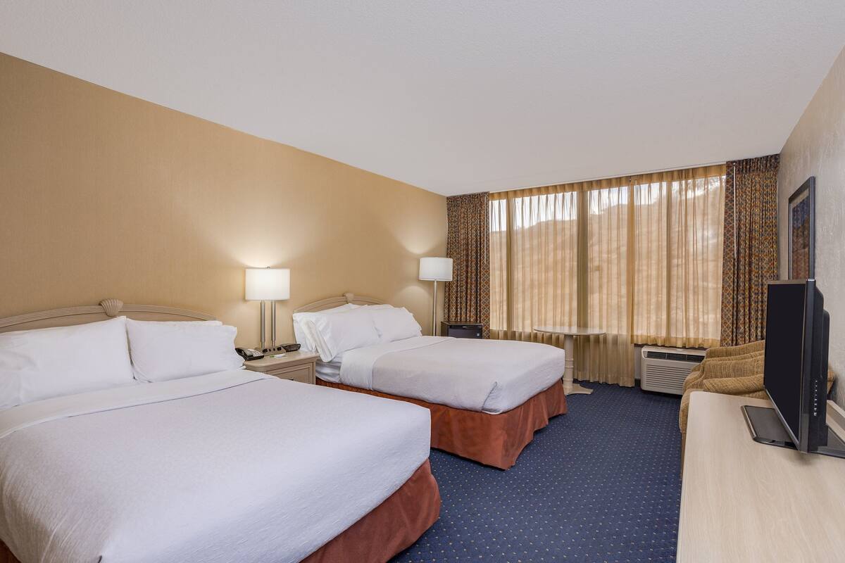 A hotel room with two beds, a desk, a television, and a window with curtains.
